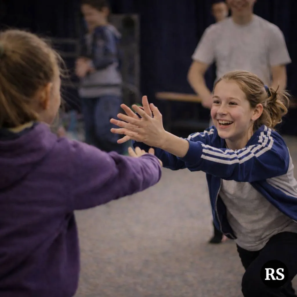 Students laughing and high-fiving during drama warm-up game at Ranges Studio