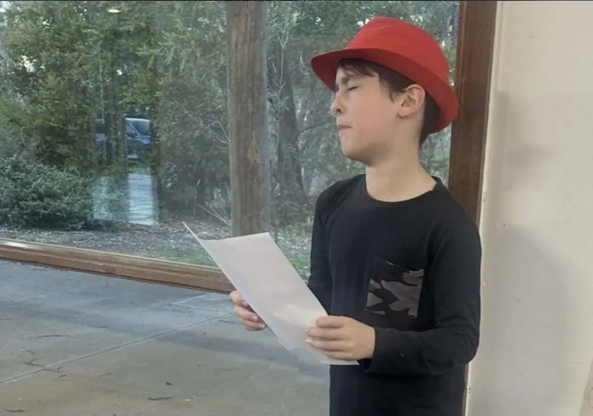 Student in a red hat reading a script during a speech and drama class