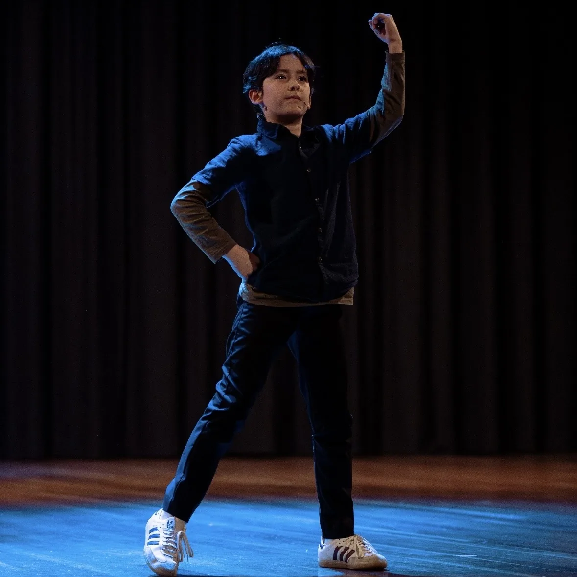 Speech and drama student mid-gesture on stage with one arm raised