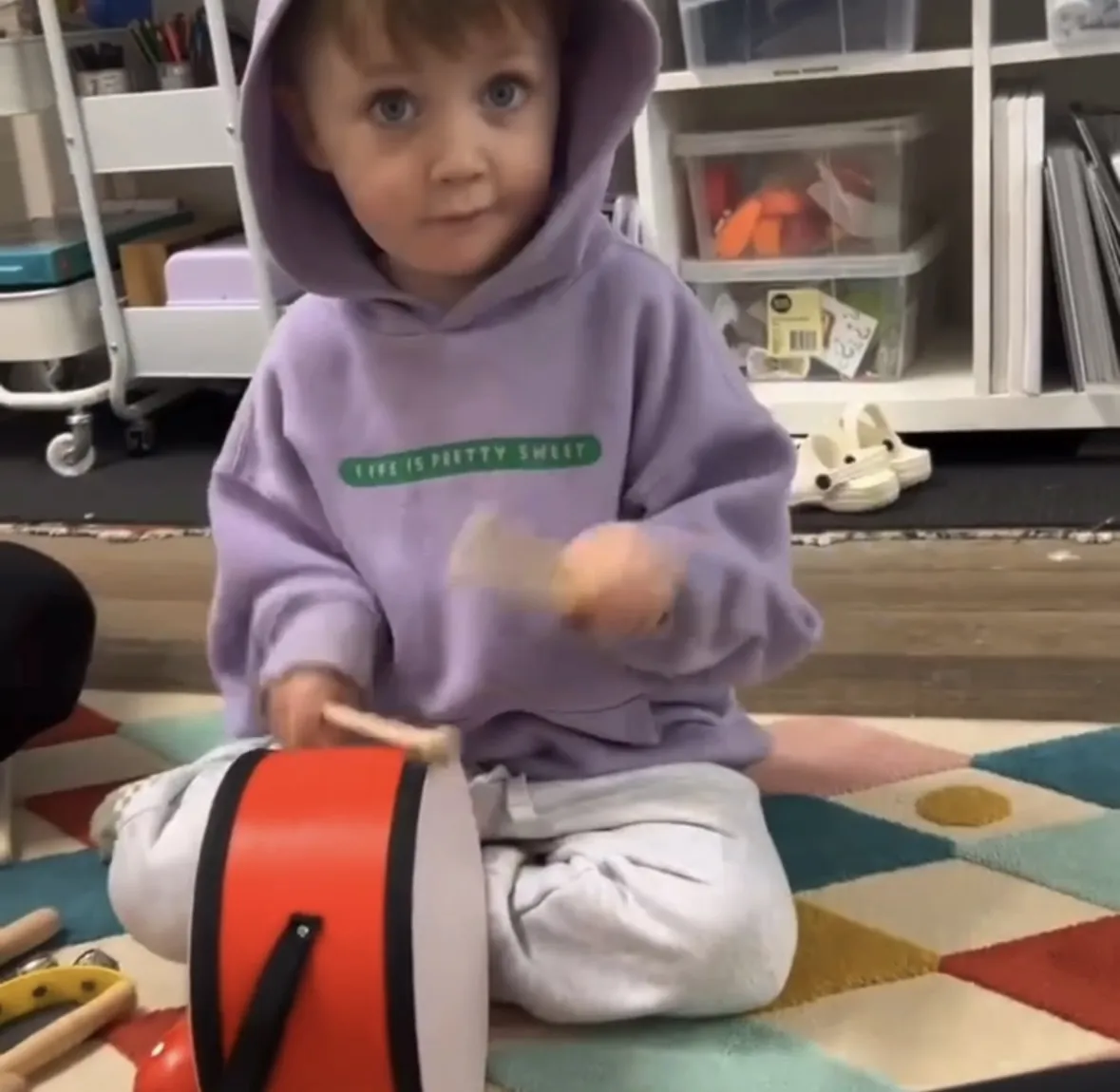 Toddler in blue playing a drum during a Tell & Show music session