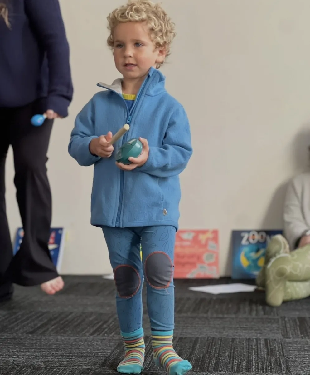 Young children playing percussion instruments on the floor at a Tell & Show class