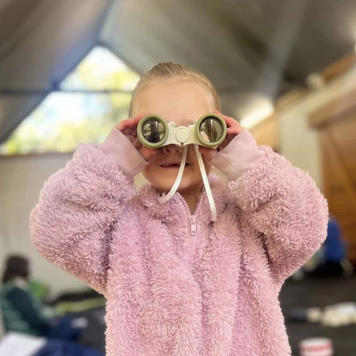 Young child in a pink coat peering through toy goggles during imaginative play