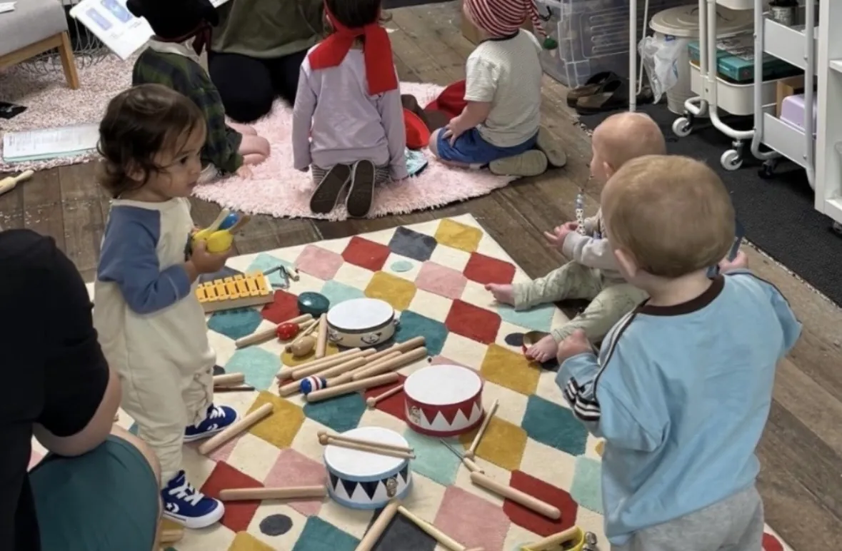 Group of young children playing instruments together on the floor at a Tell & Show class