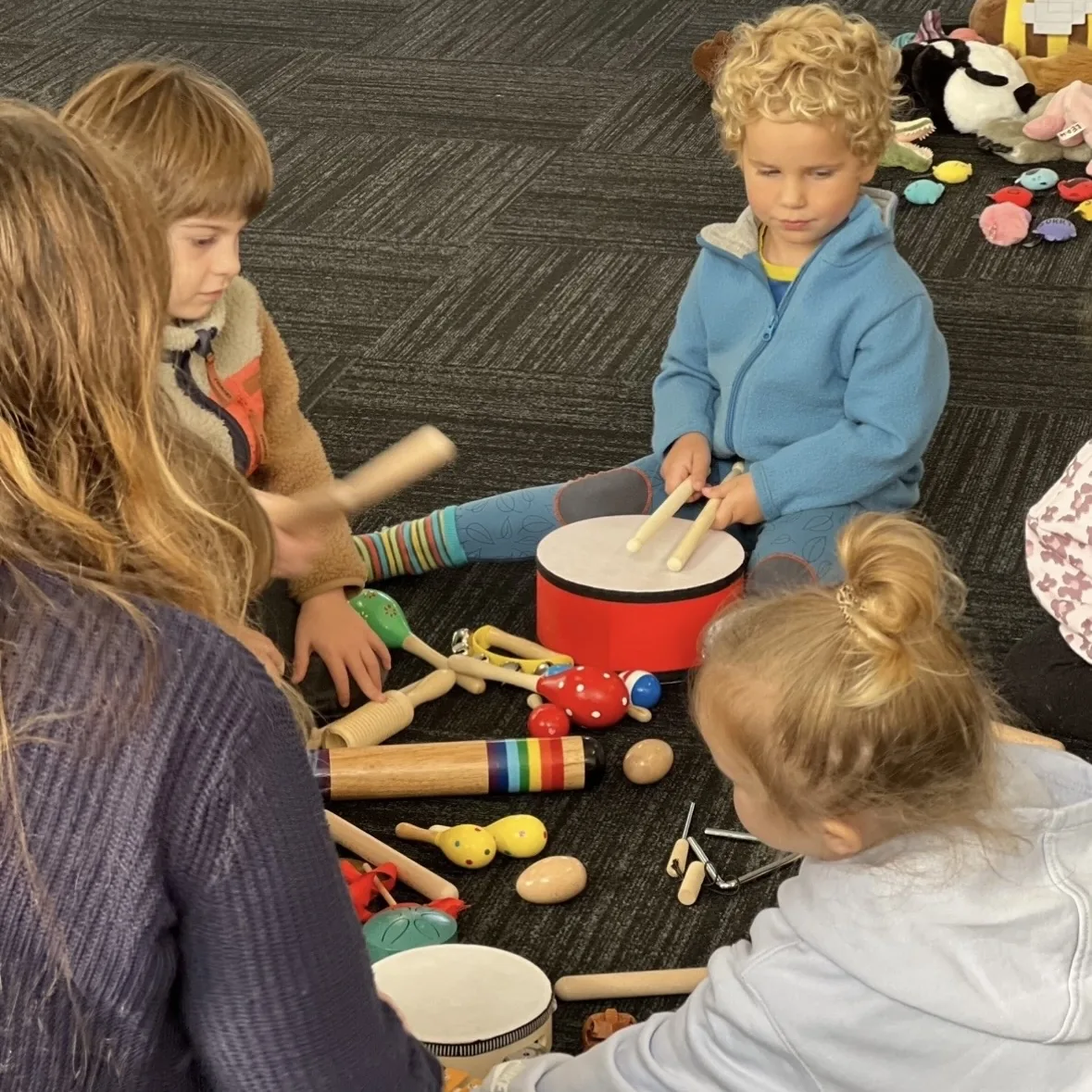 Early learners making music together with drums and percussion at a Tell & Show class