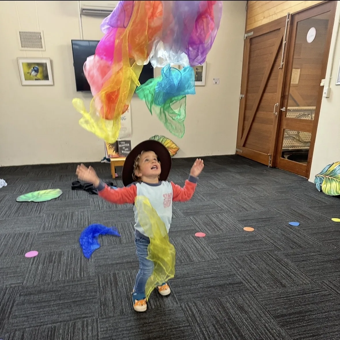 Young child throwing colourful scarves into the air at a Tell & Show class