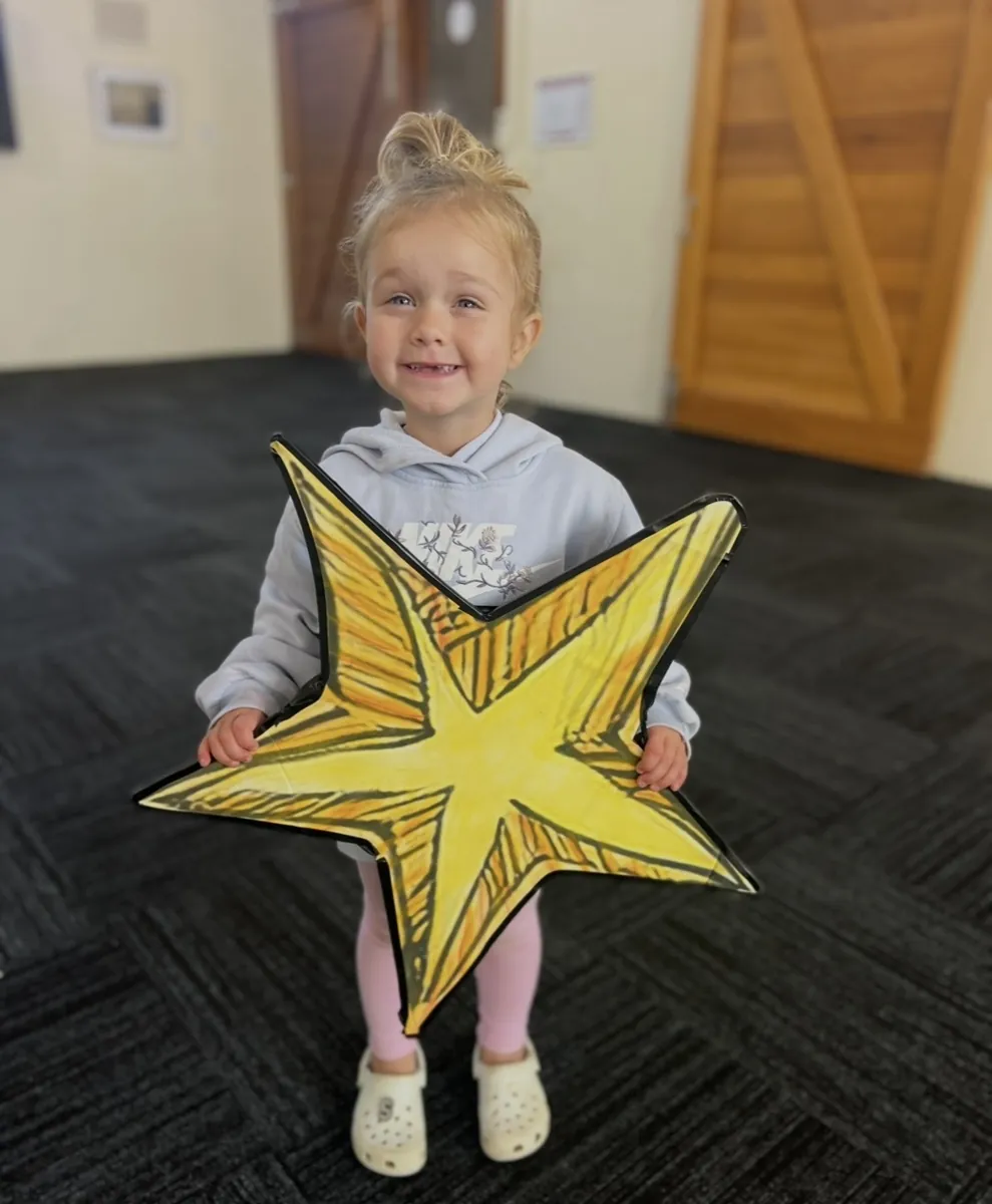 Young child holding a glowing star prop during imaginative play at a Tell & Show class
