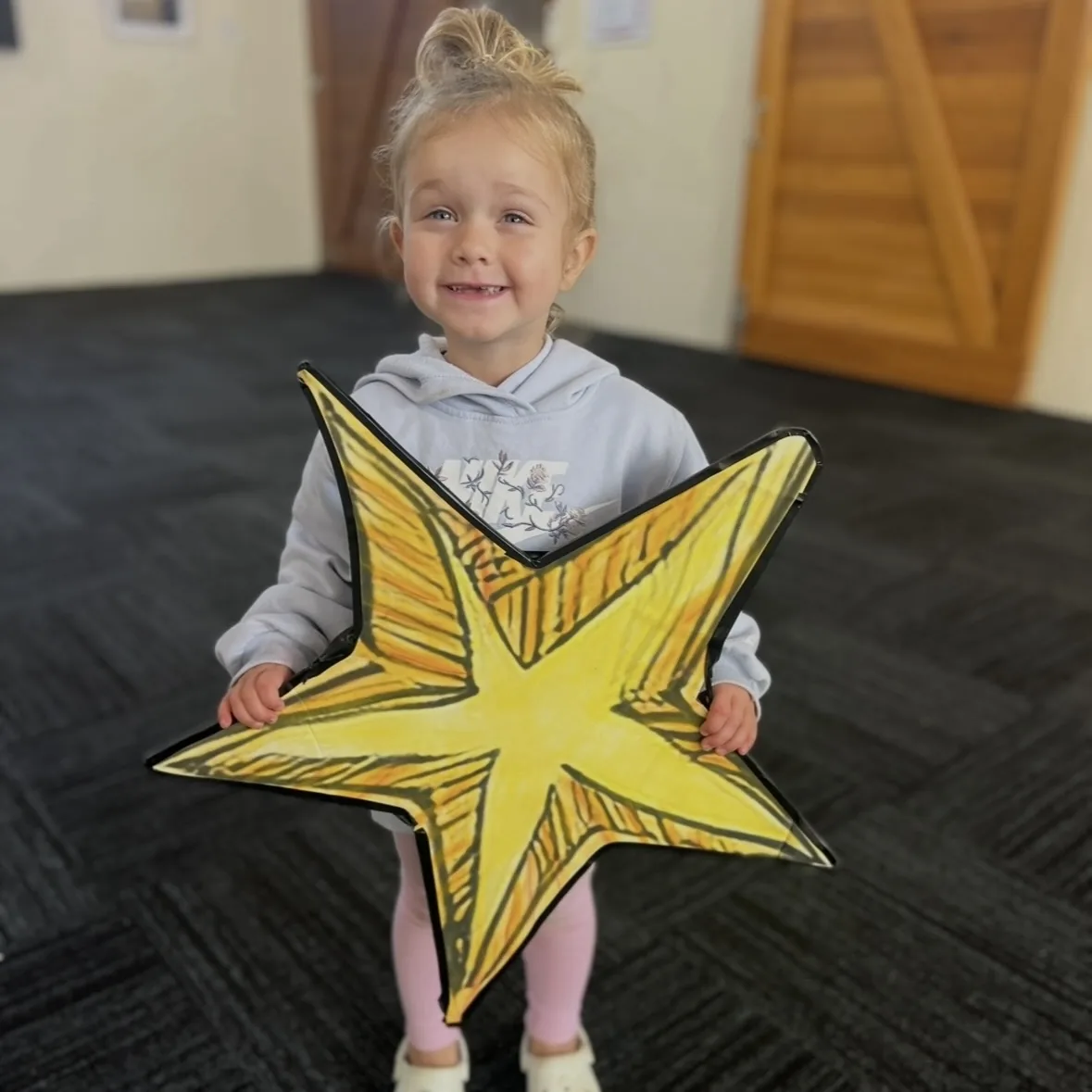 A beaming toddler holding a large paper star during a Tell & Show class