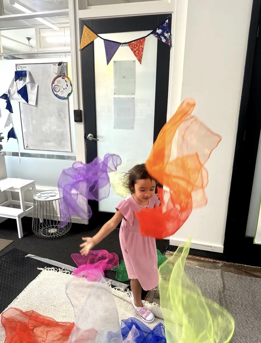 Young child wrapped in colourful streamers during imaginative play at a Tell & Show class