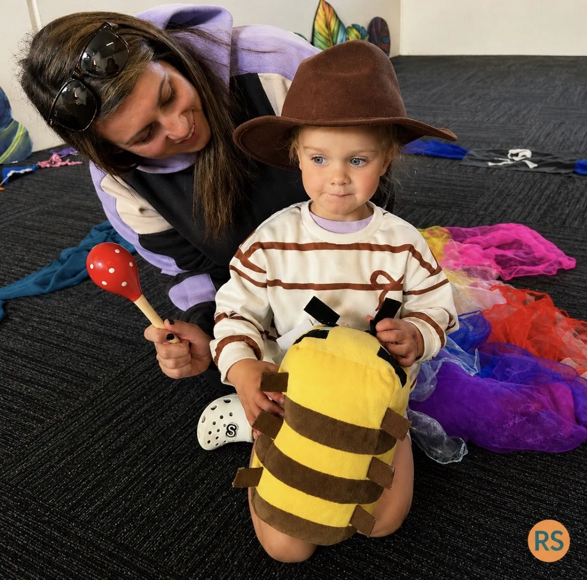 Teacher helping a young child in costume with colourful scarves at a Tell & Show class